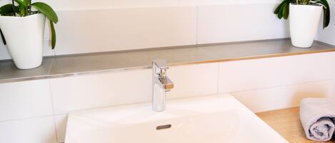 A bathroom with a white sink, a mirror, and two potted orchids.