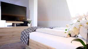 Une chambre moderne avec un grand lit, un téléviseur à écran plat et une orchidée en pot.