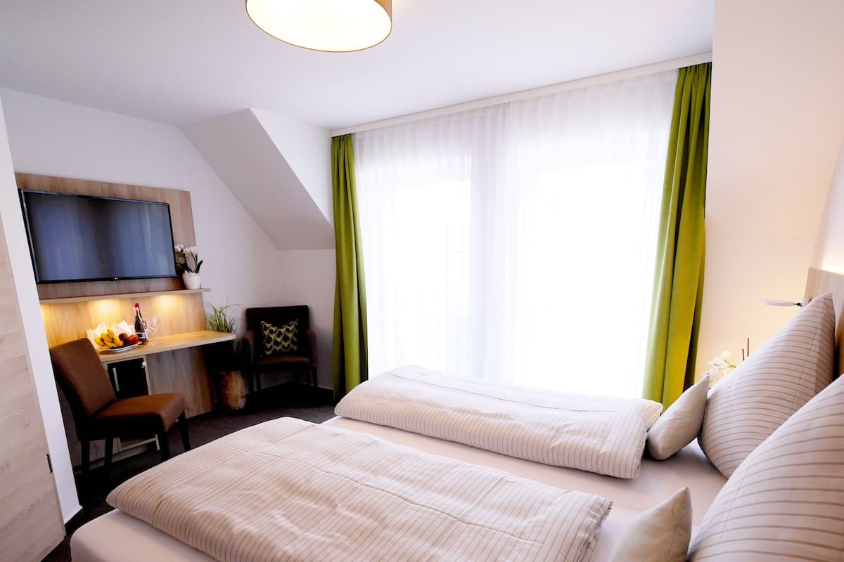 Een hotelkamer met twee bedden, een bureau, een stoel, een televisie en een raam met gordijnen.