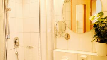 A bathroom with a shower, a sink, a mirror, and a potted plant.
