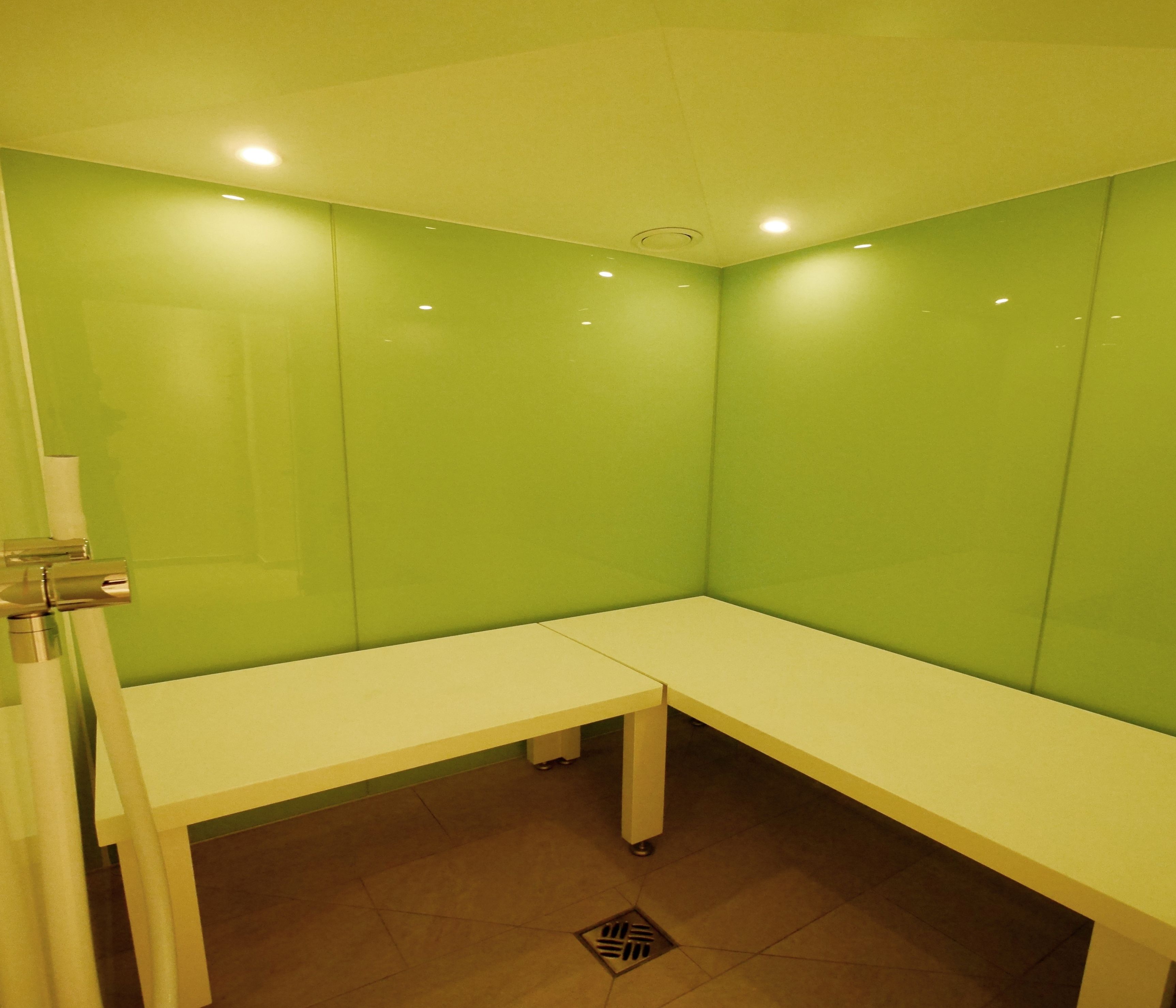 A small, enclosed room with green walls, a white bench, and a door.