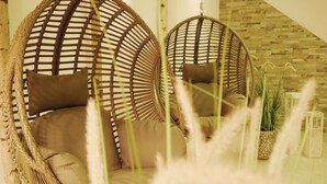 Deux fauteuils suspendus en osier avec des coussins, une plante en pot et un escalier avec un mur en bois.