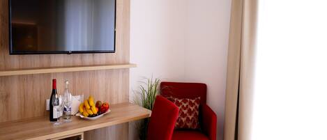 Un salón moderno con un televisor de pantalla plana montado en una pared de madera, un sillón rojo, una mesita de madera con un frutero, botellas de vino y copas.