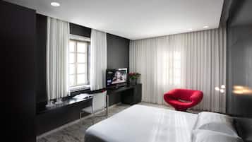 A modern hotel room with a large bed, a desk with a computer, a red chair, and a TV.