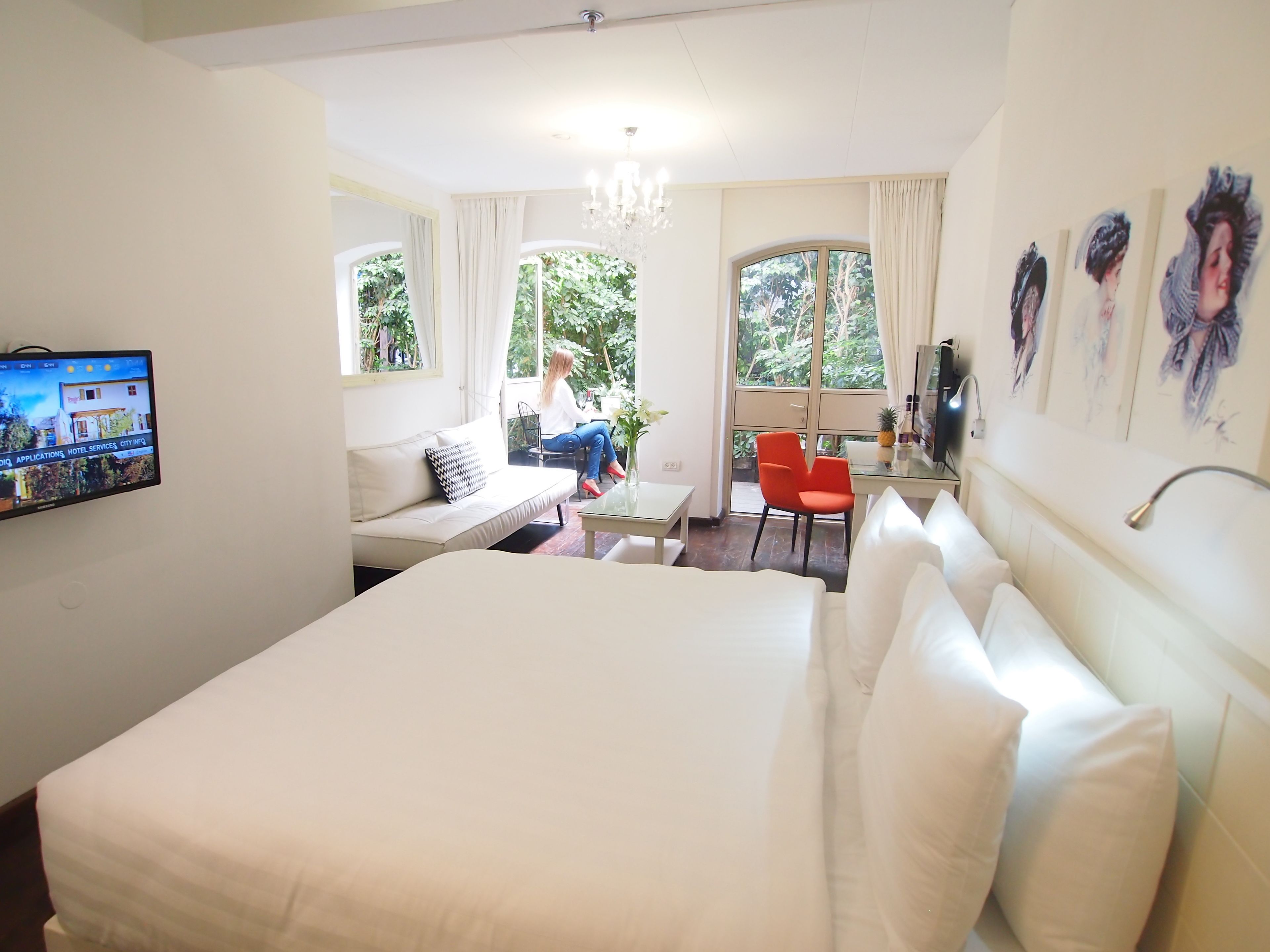 A hotel room with a large bed, a desk, a red chair, a TV, and a window with curtains.