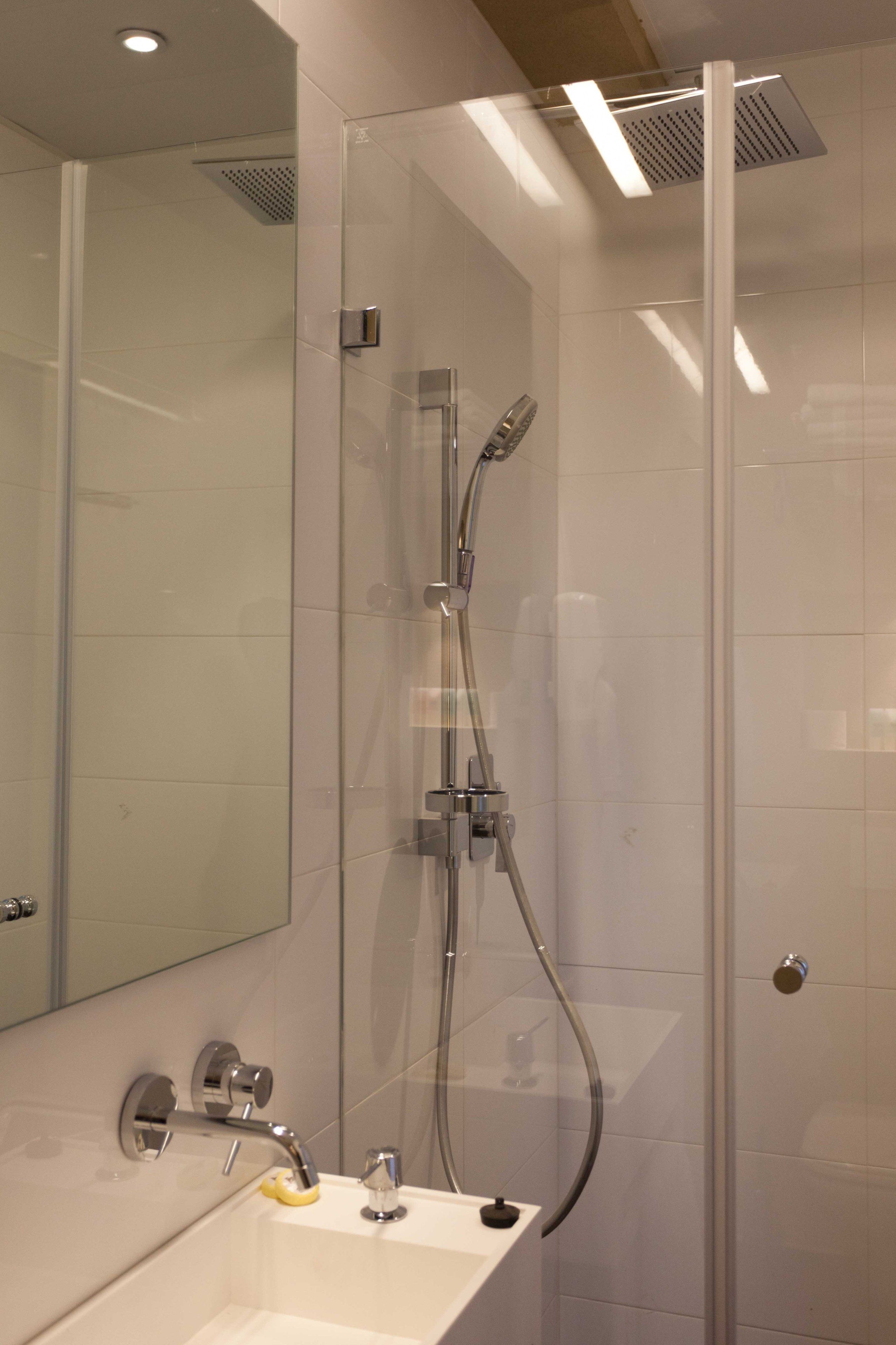 A modern bathroom with a glass-enclosed shower, a sink with a yellow soap dispenser, and a mirror.