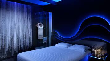 Un dormitorio moderno con separador de vidrio, una cama y una mesita de noche con una botella y vasos.