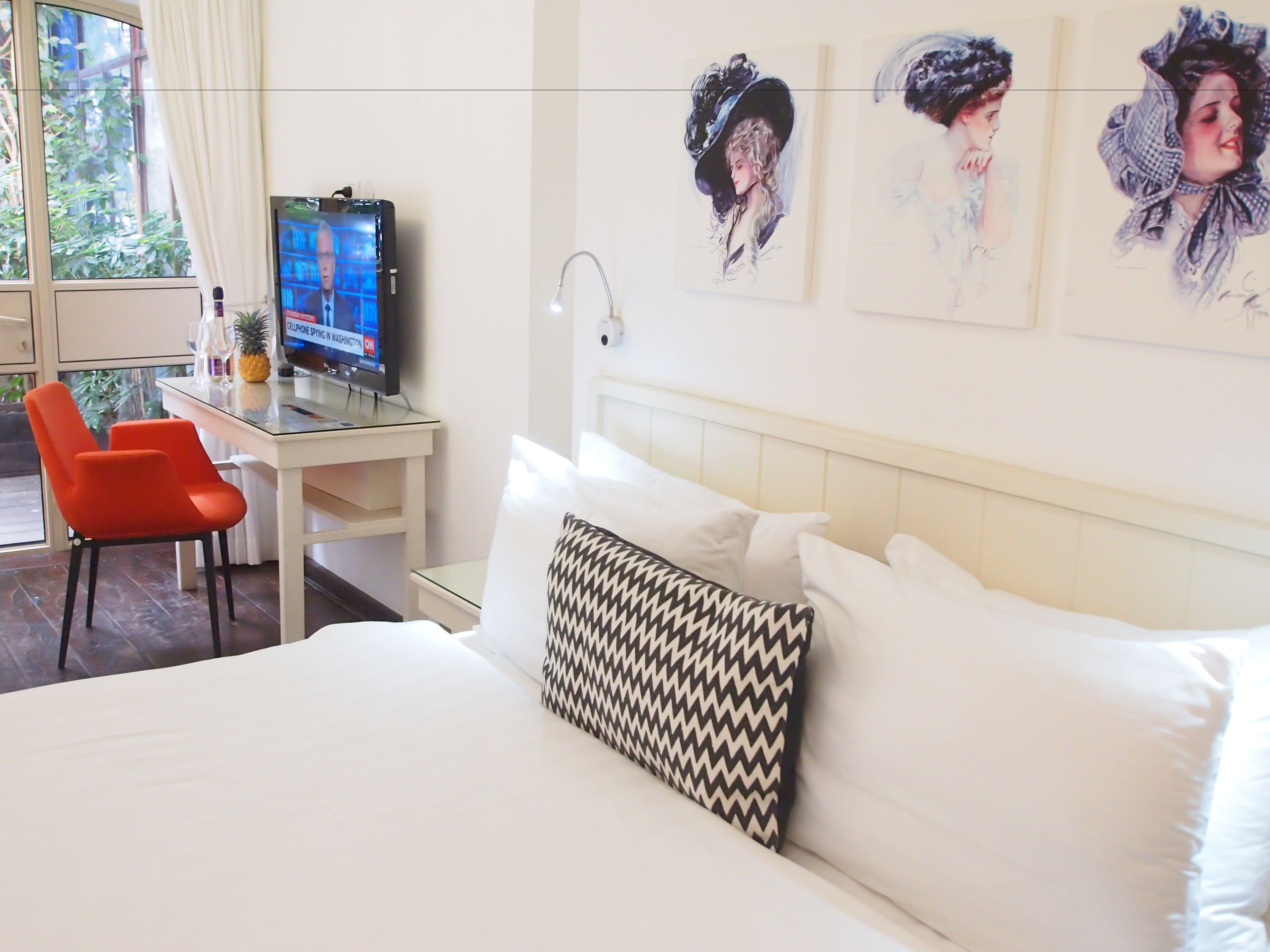 A hotel room with a bed, a desk with a computer, a chair, and artwork on the wall.