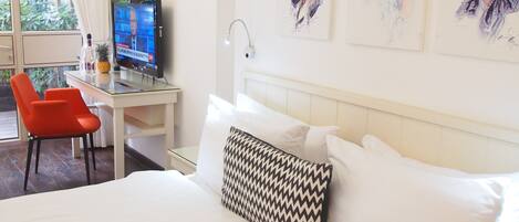 A hotel room with a bed, a desk with a computer, a chair, and artwork on the wall.