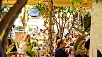 An outdoor dining area with wicker chairs and tables, surrounded by greenery and hanging decorations.