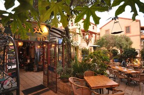 An outdoor cafe with wooden tables and chairs, surrounded by potted plants and a building with a sign. - Templers Boutique Hotel (Haifa)