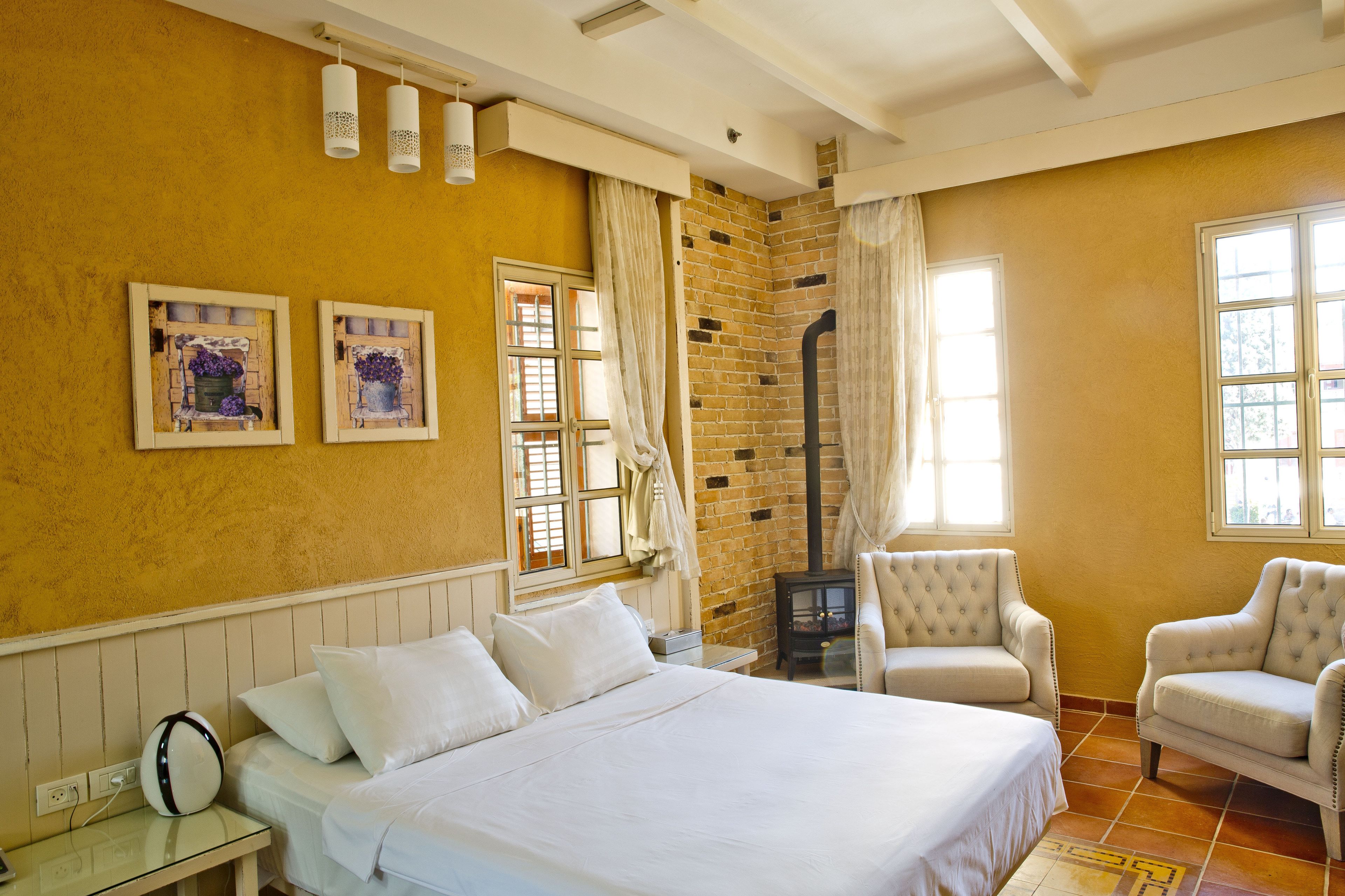 A hotel room with a large bed, two armchairs, a small table, and a fireplace.