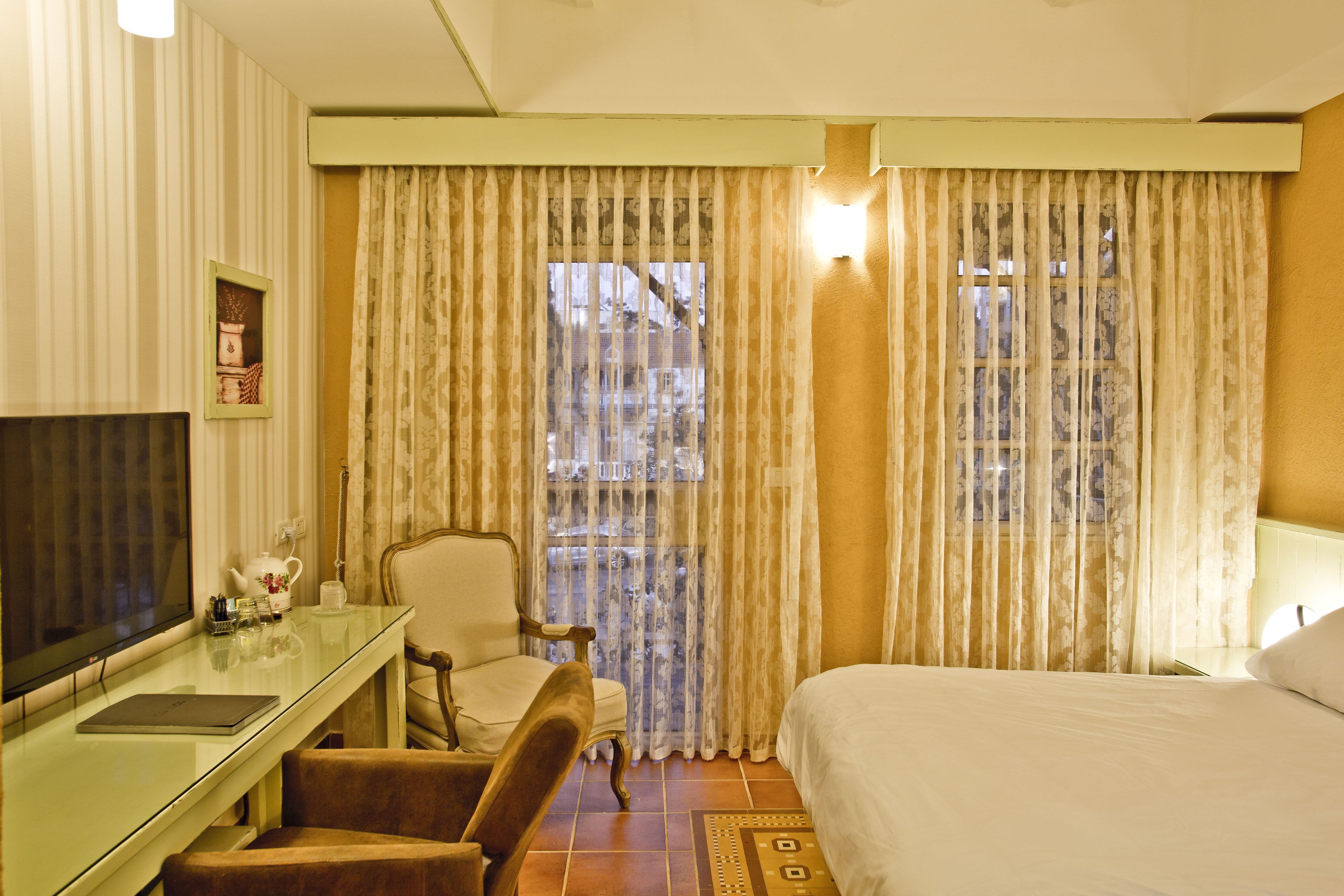 A hotel room with a bed, a desk with a chair, a television, and curtains.