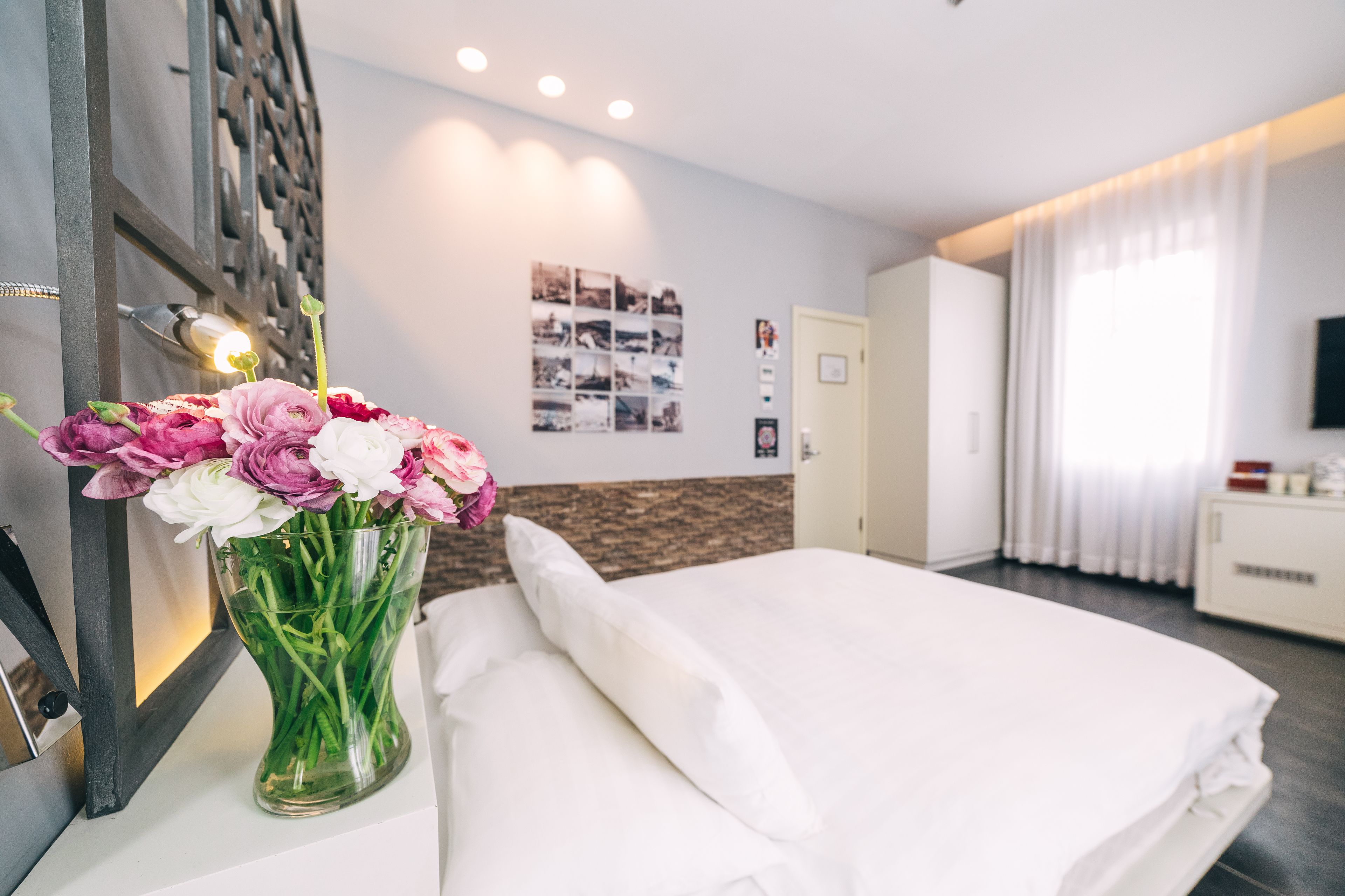 A hotel room with a bed, a vase of flowers, a wall-mounted TV, and a framed photo.
