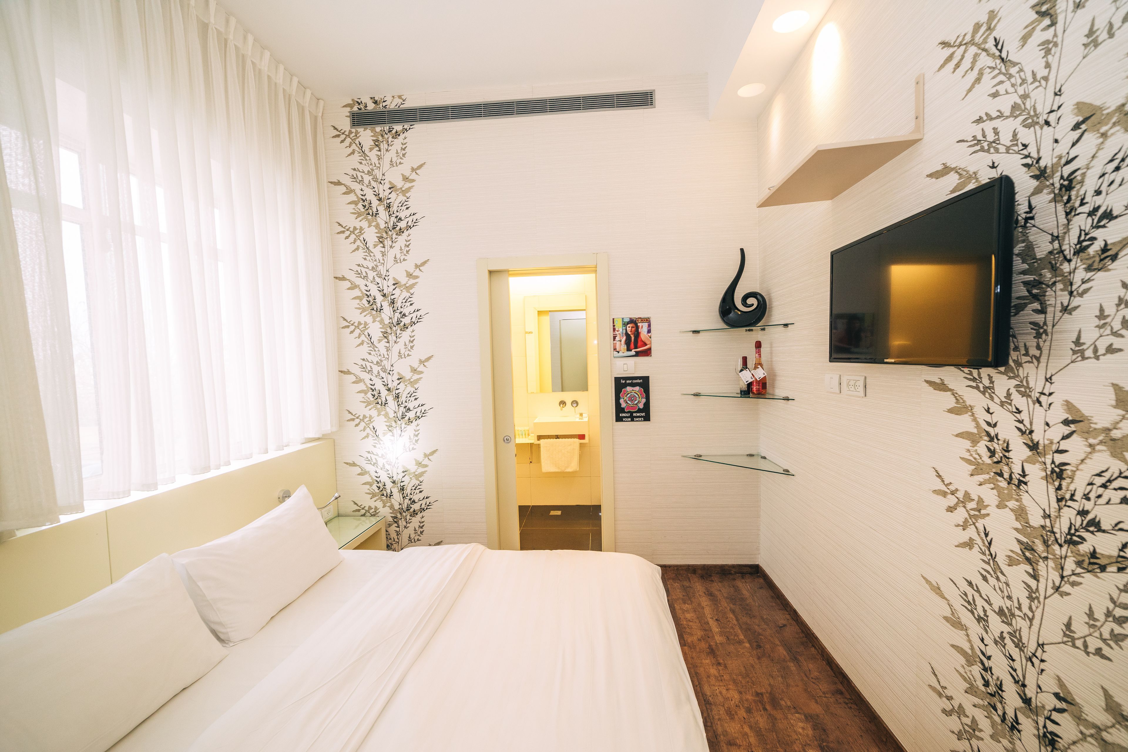 A hotel room with a bed, a TV mounted on the wall, a small bathroom, and a wooden floor.