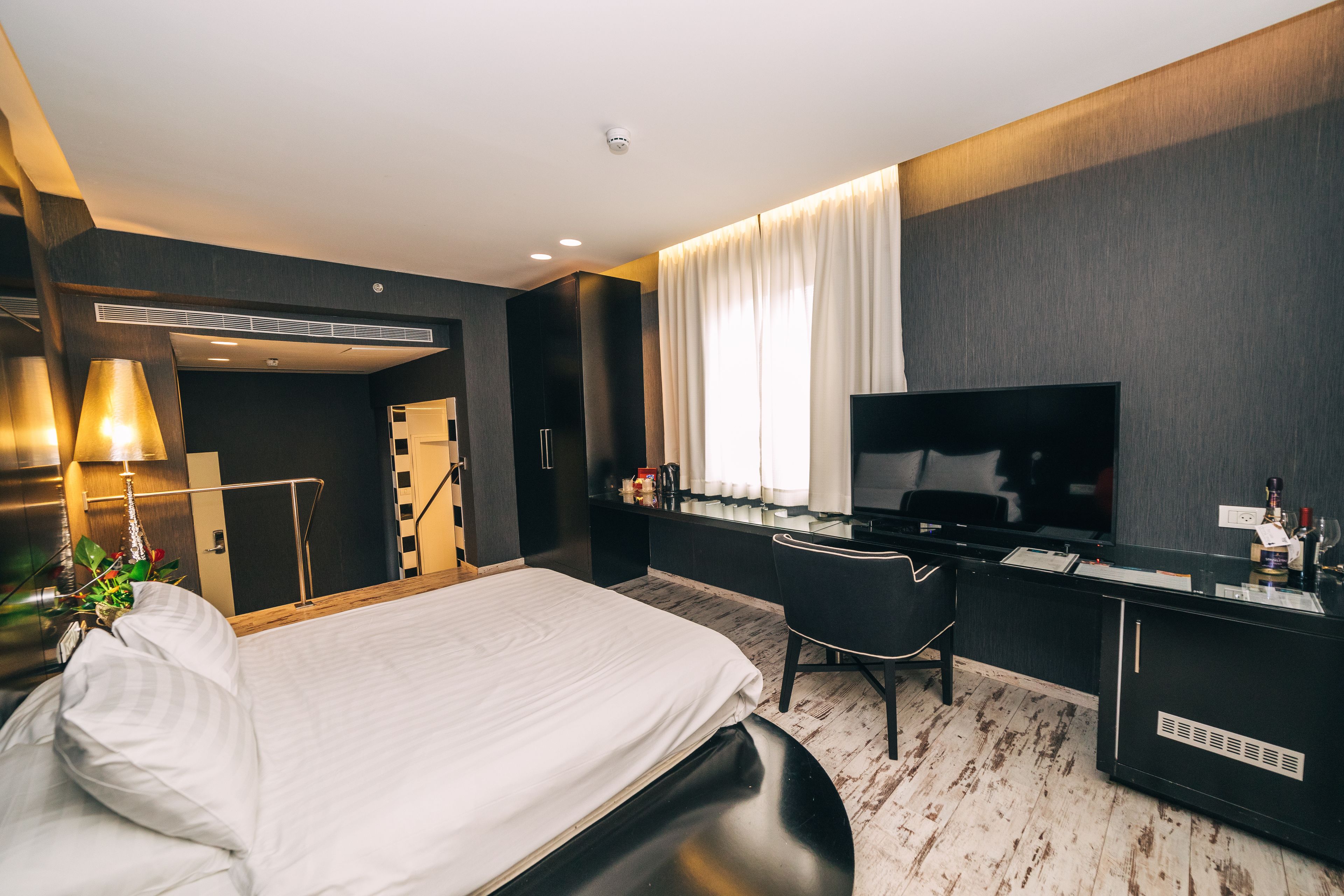 A modern hotel room with a bed, desk, and television.