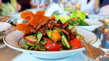 A salad with various vegetables and a piece of meat, served on a white plate with a patterned rim.