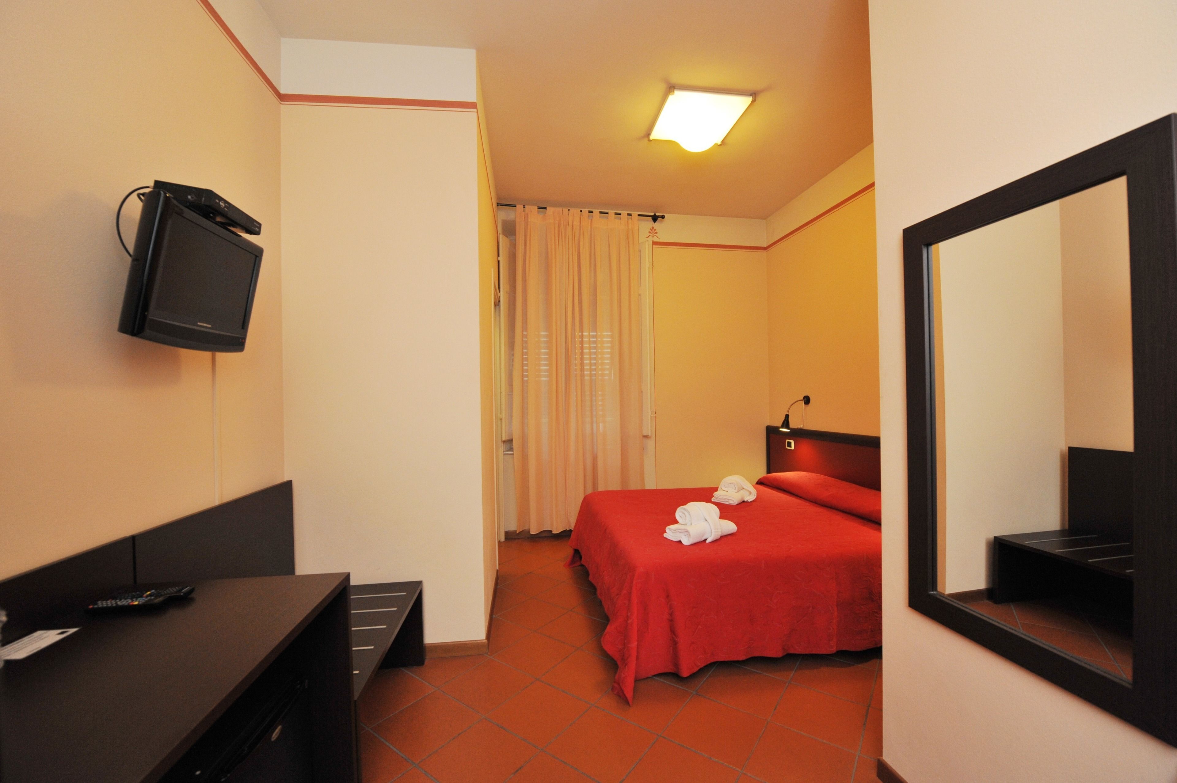 A hotel room with a bed, a TV mounted on the wall, a desk with a remote control, and a mirror.