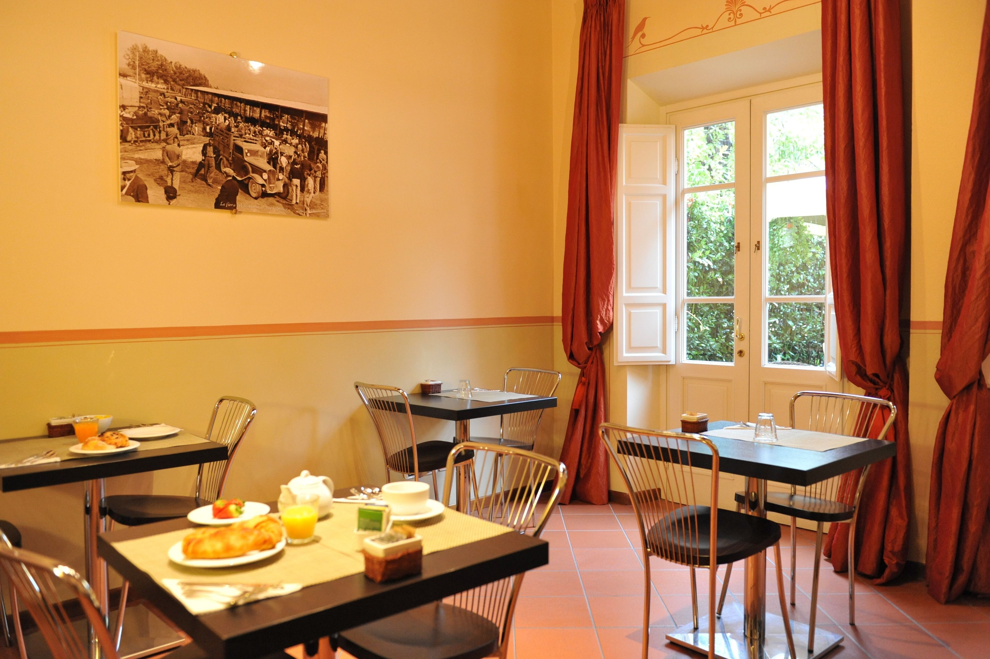 Comedor con mesas y sillas, alimentos para el desayuno y una ventana con cortinas.