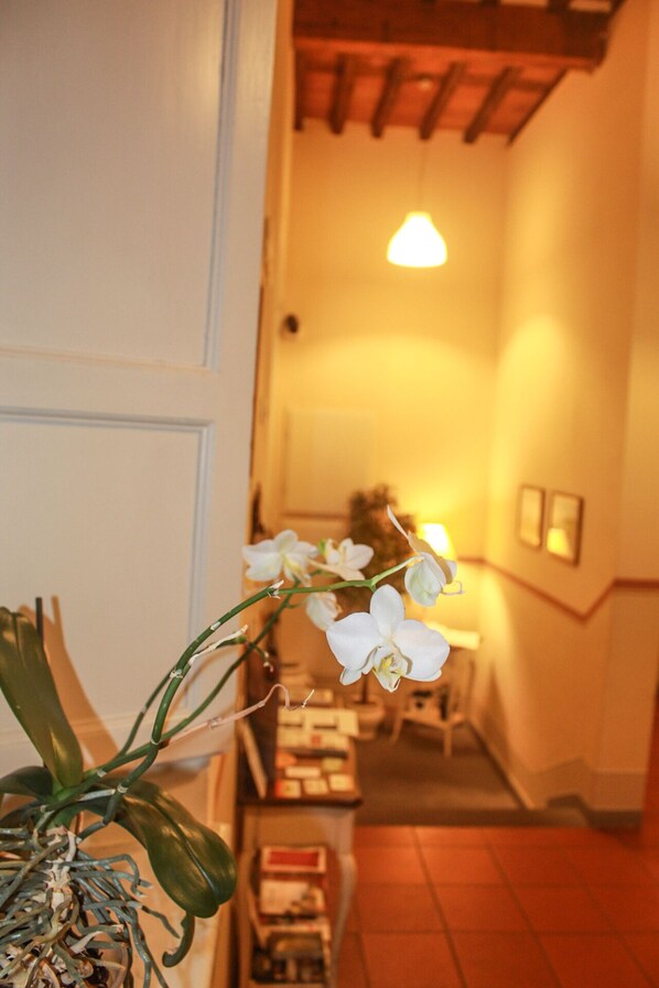 A hallway with a staircase, a vase with white flowers, and a warm light fixture. - Il Seminario Bed and Breakfast (Lucca)