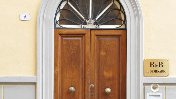 Una puerta doble de madera con una celosía metálica, un letrero con el número '2' encima y una placa que dice 'B&B IL SEMINARIO'.
