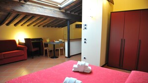 Una habitación de hotel con una cama, un sofá rojo, una mesa de comedor con sillas y un armario.