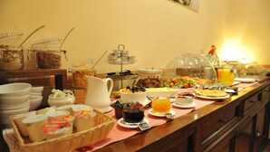 Un bufé con diversas opciones de comida y bebidas, incluyendo una estación de café, fruta, pastelería y un dispensador de zumo.