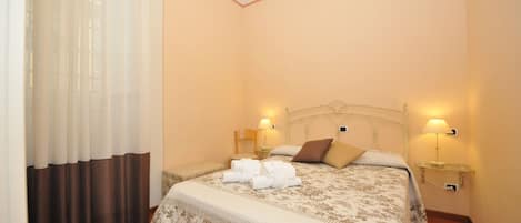 A neatly made bed with a floral bedspread, two bedside lamps, and a pair of folded towels on the bed.
