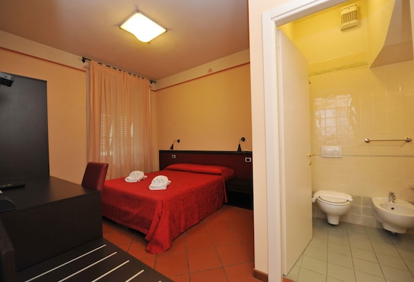 Habitación de hotel con cama, escritorio, silla y baño con inodoro y bidé.