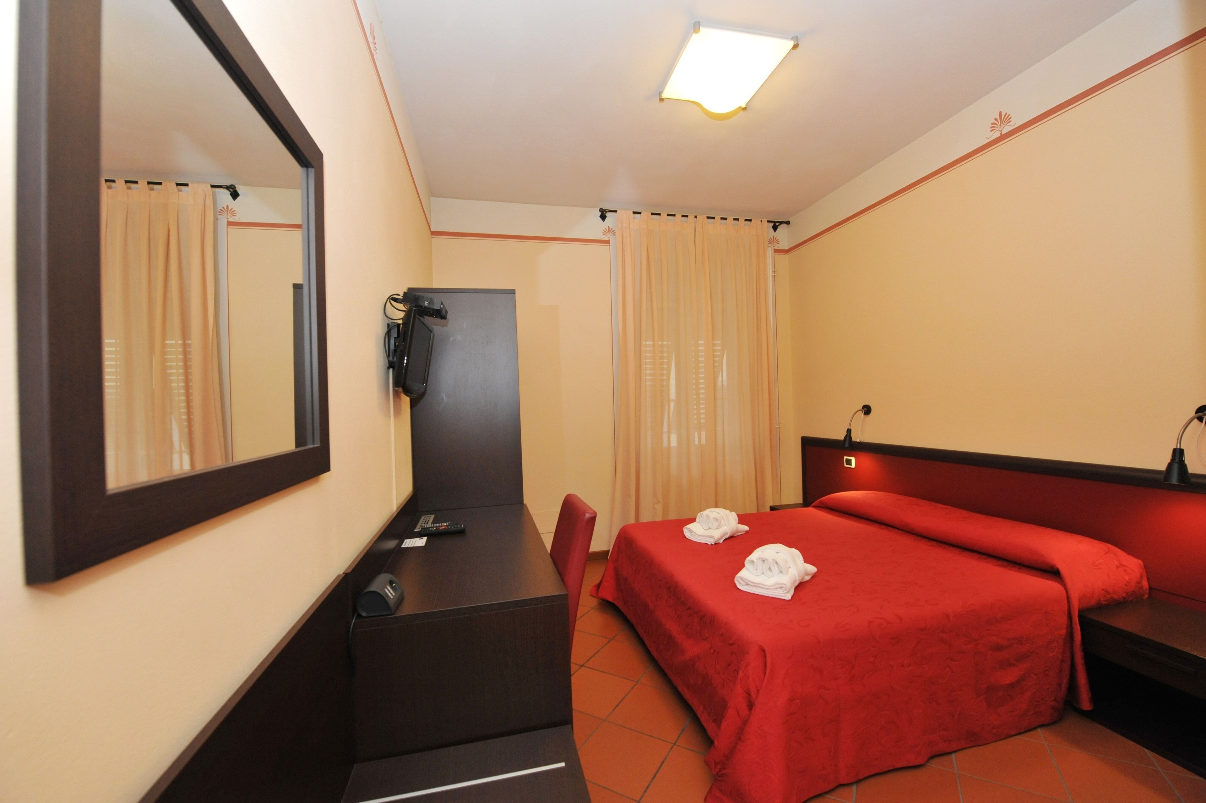 Een hotelkamer met een bed, bureau, stoel, spiegel, telefoon en gordijnen.