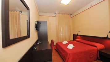 Una habitación de hotel con cama, escritorio, silla, espejo, teléfono y cortinas.