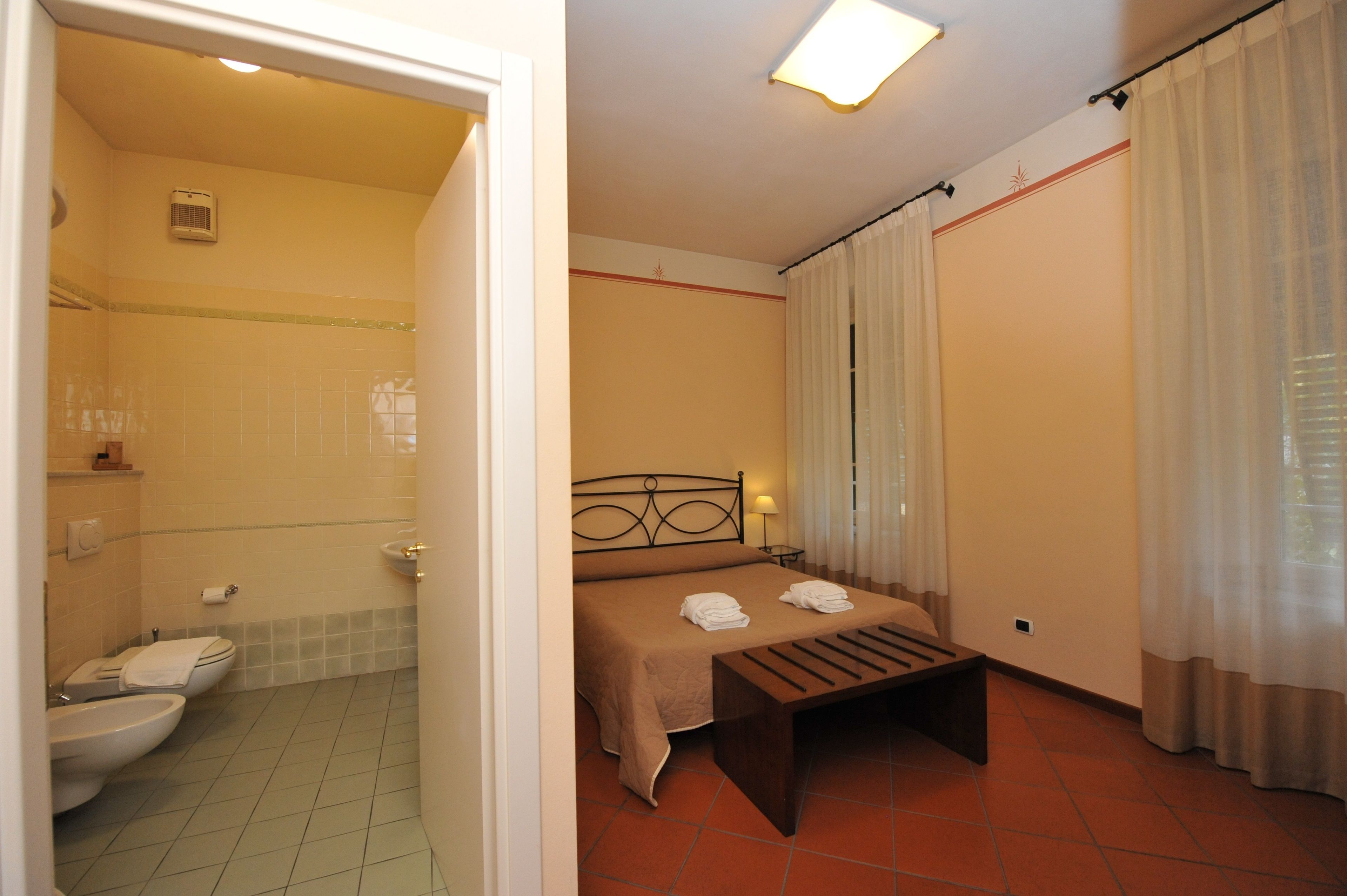 A hotel room with a bed, a bedside table, a bathroom with a toilet and sink, and a shower.