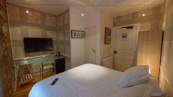 Hotelkamer met een bed, een bureau met een televisie, een radiator en een deur met een bordje.