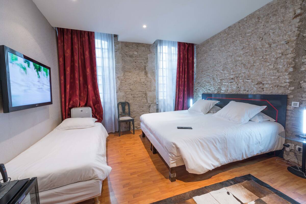 A hotel room with two beds, a stone wall, and a wooden floor.
