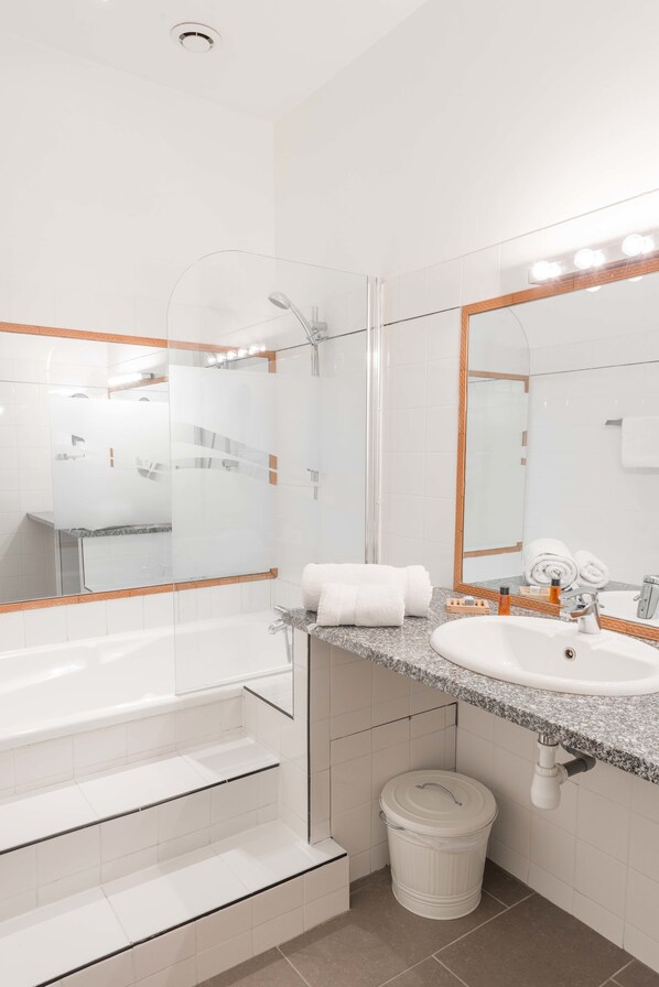 A modern bathroom with a white bathtub, a granite countertop sink, and a large mirror with a wooden frame.