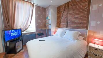 A hotel room with a large bed, a television on a stand, a brick wall, and a window with curtains.