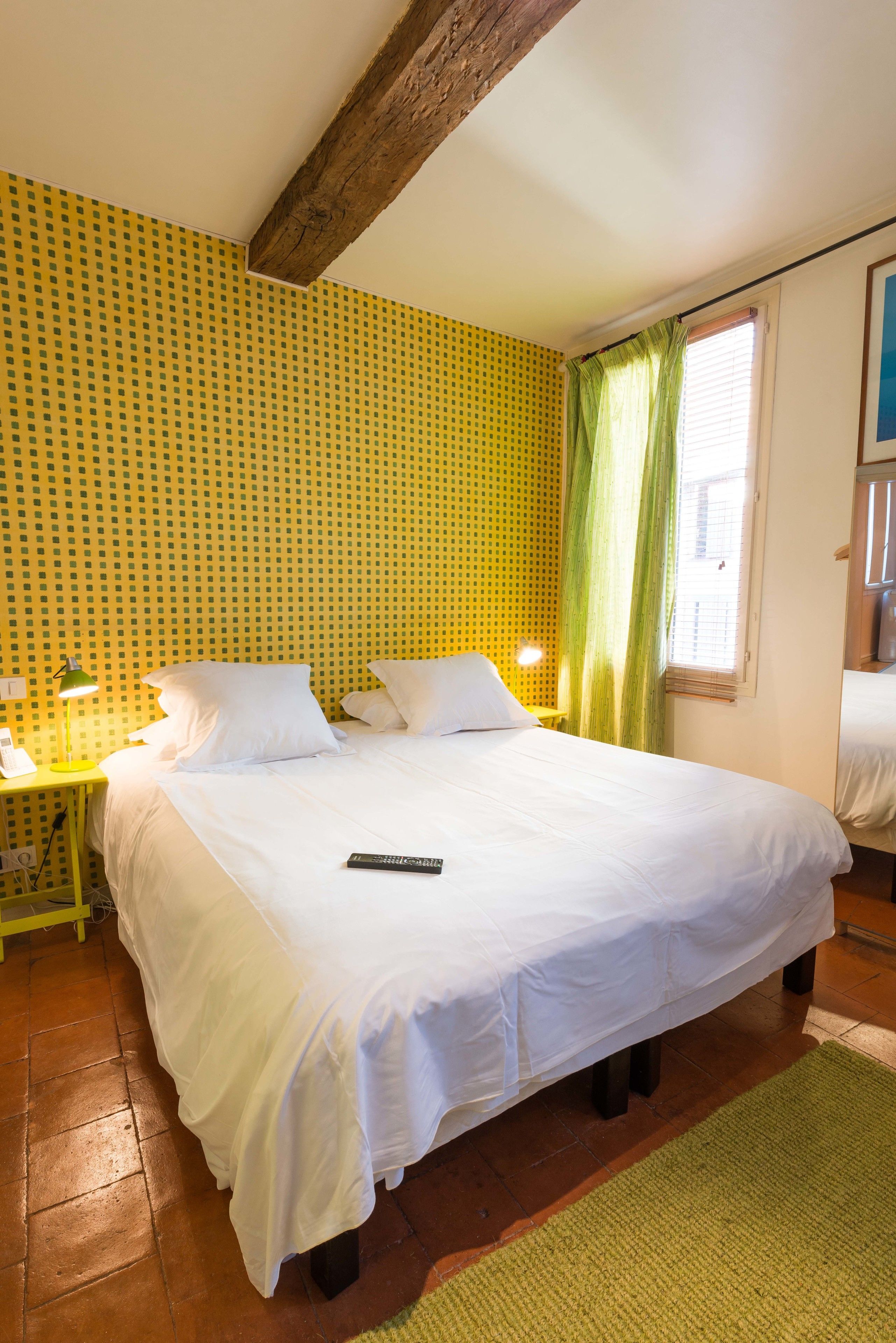 Una cama con sábanas blancas, una cortina verde y un papel tapiz amarillo con estampado.
