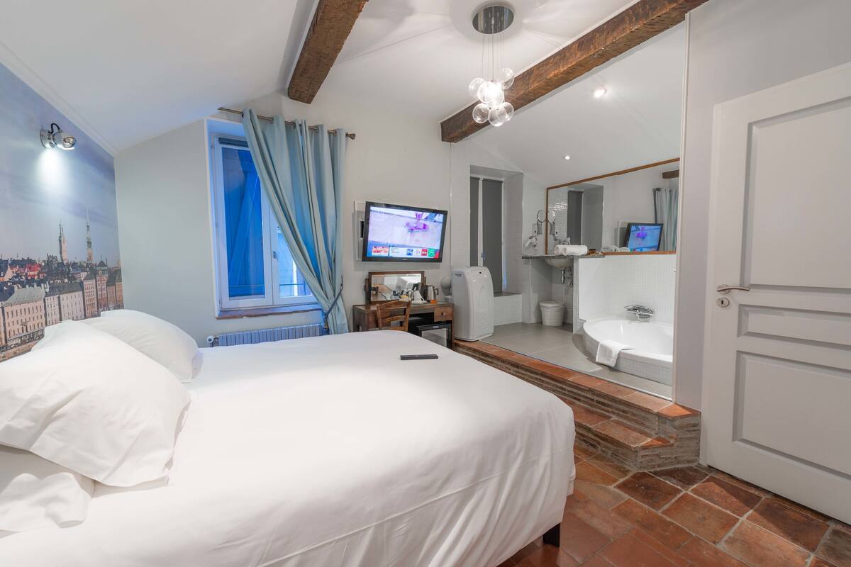A hotel room with a bed, a desk, a television, a bathroom with a bathtub, and a cityscape mural on the wall.