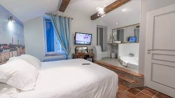 Een hotelkamer met een bed, een bureau, een televisie, een badkamer met een bad en een stadsgezicht muurschildering op de muur.
