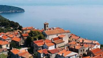 A coastal village with terracotta-roofed buildings, a prominent tower, and a view of the sea.
