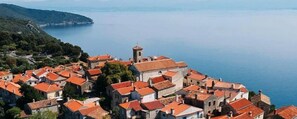 A coastal village with terracotta-roofed buildings, a prominent tower, and a view of the sea.