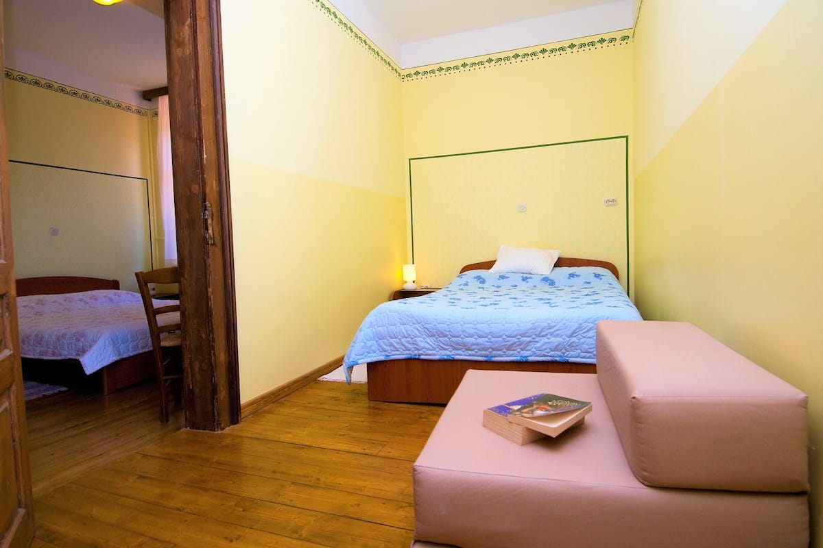 A bedroom with a bed, a bedside table with a lamp, a chair, and a pink ottoman.