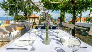 An outdoor dining area with tables set for a meal, a vase with flowers, and a view of the sea. - Pansion Tramontana (Cres)