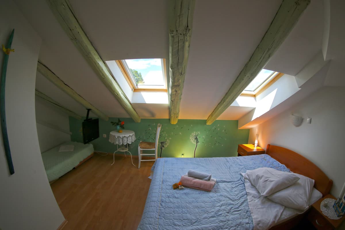 A bedroom with a skylight, a bed, a chair, a small table, and a lamp.