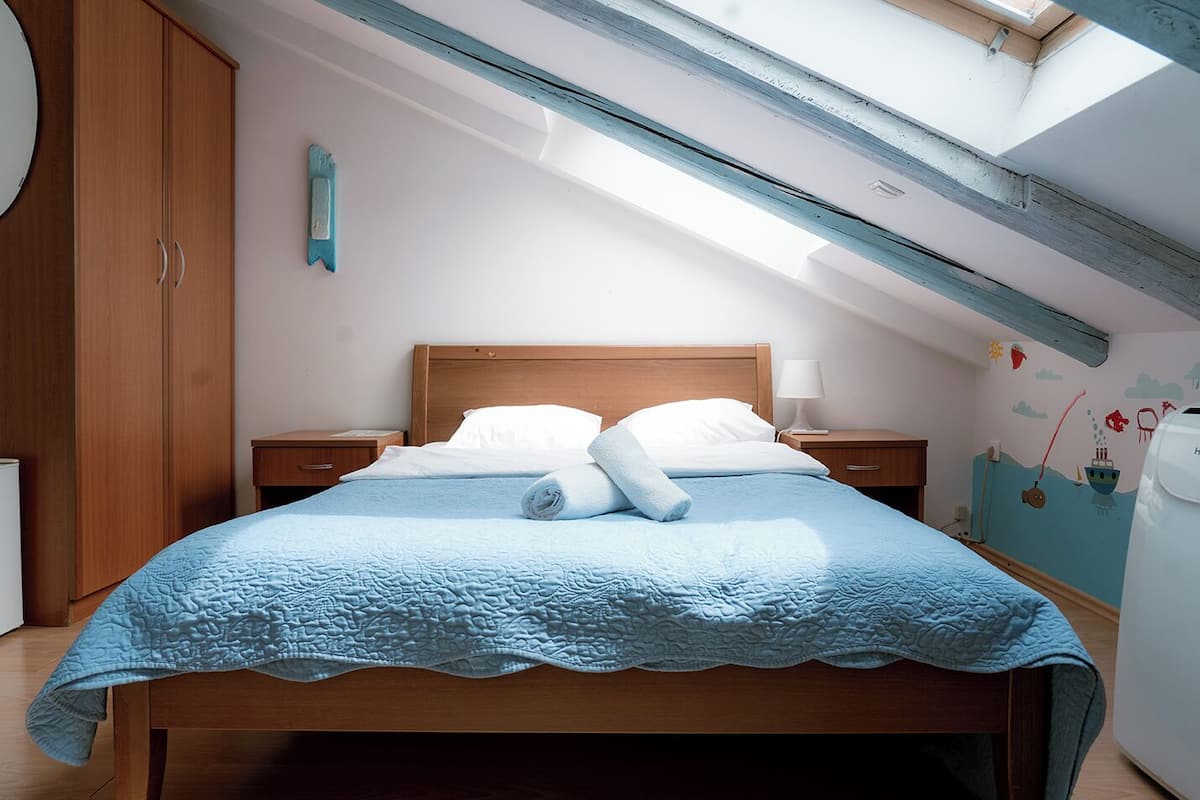 A bedroom with a skylight, wooden bed frame, two bedside tables, and a wall mural.