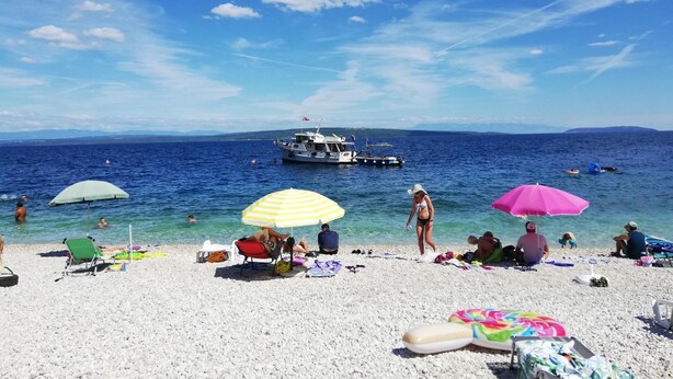 A beach with clear blue water, a boat in the distance, and people relaxing on the sand. - Pansion Tramontana (Cres)