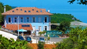 A two-story building with a tiled roof, a visible entrance, and a view of the sea in the background. - Pansion Tramontana (Cres)