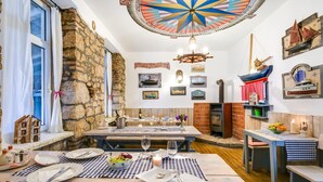 A cozy dining area with a stone wall, a wooden table set for two, and a ceiling with a colorful compass design. - Pansion Tramontana (Cres)