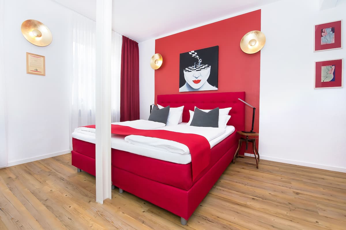 Ein modernes Schlafzimmer mit einem roten Bett, weißen Wänden und einem Holzboden.