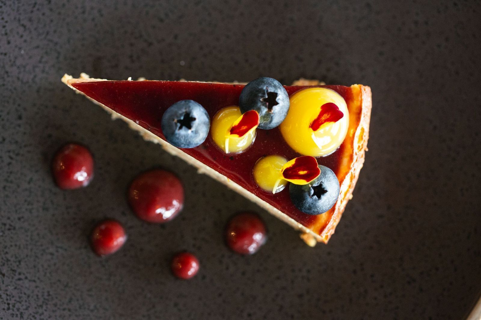 Une part de tarte aux myrtilles, recouverte d’une garniture jaune, et entourée de myrtilles éparpillées.
